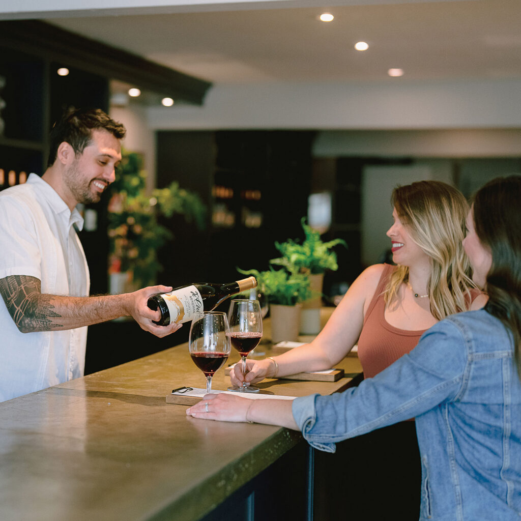 Tasting room associate pouring Benziger De Coelo pinot noir to two guests
